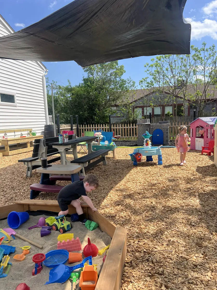 The fenced outdoor yard with shaded sandbox, water tables, and picnic benches