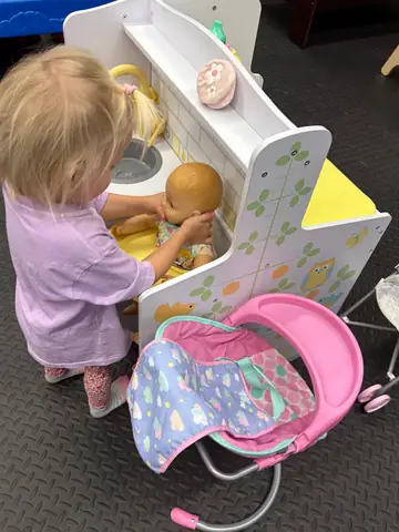 A toddler caring for a baby doll at the nursery station
