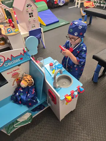 A child in doctor dress-up playing at the pretend doctor center