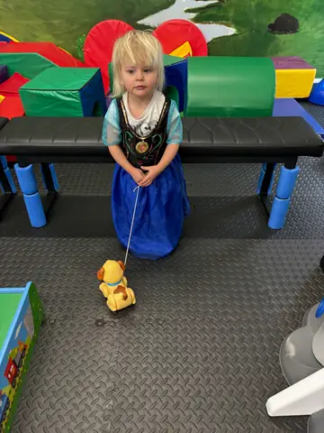 A child in a princess costume pulling a toy past the soft-play blocks