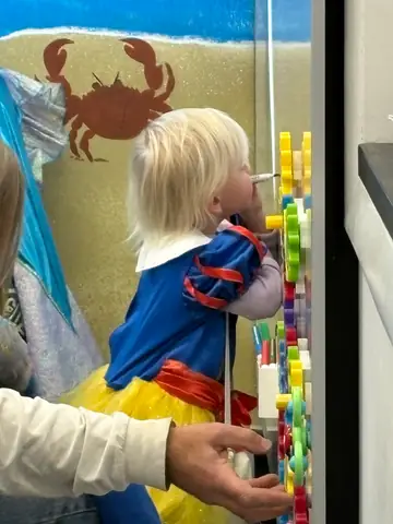 A child in a Snow White costume playing at the light-up peg wall by the beach mural