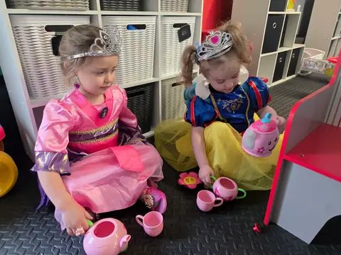Two children in princess dress-up costumes having a pretend tea party