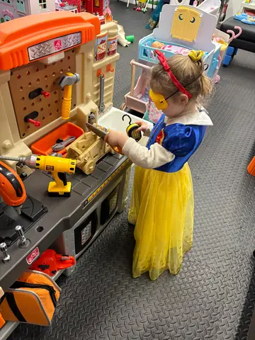 A child in a princess dress working at the tool bench