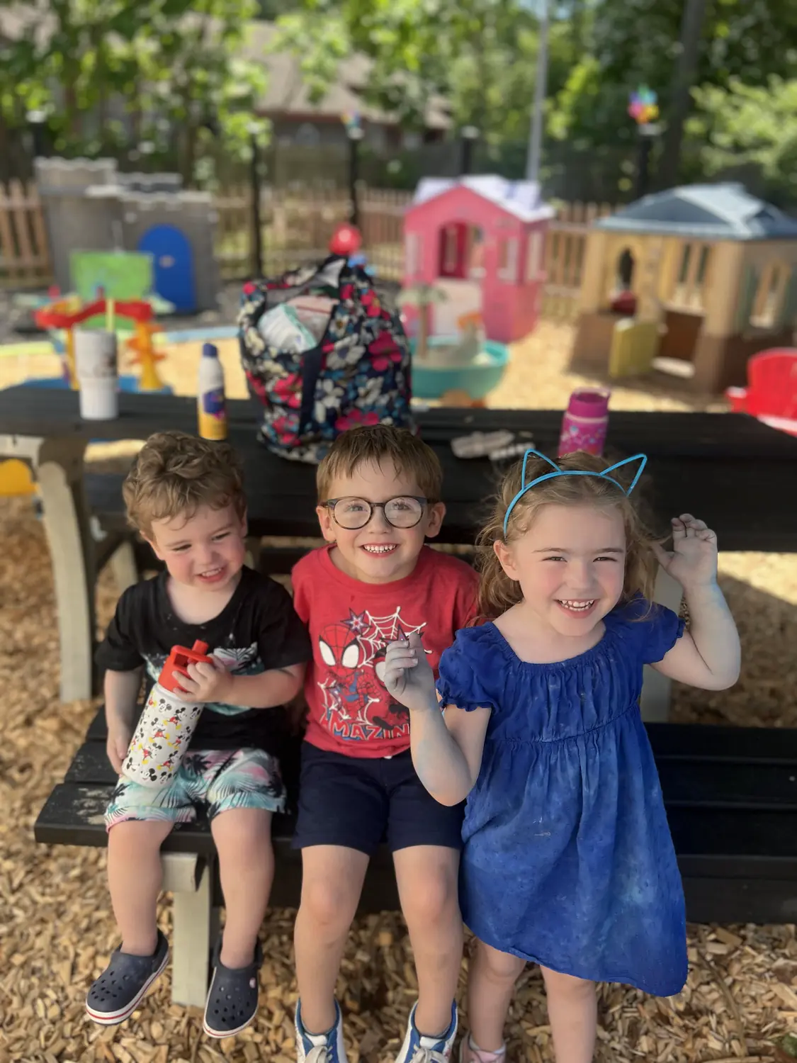 Children smiling on a picnic bench in the outdoor play yard