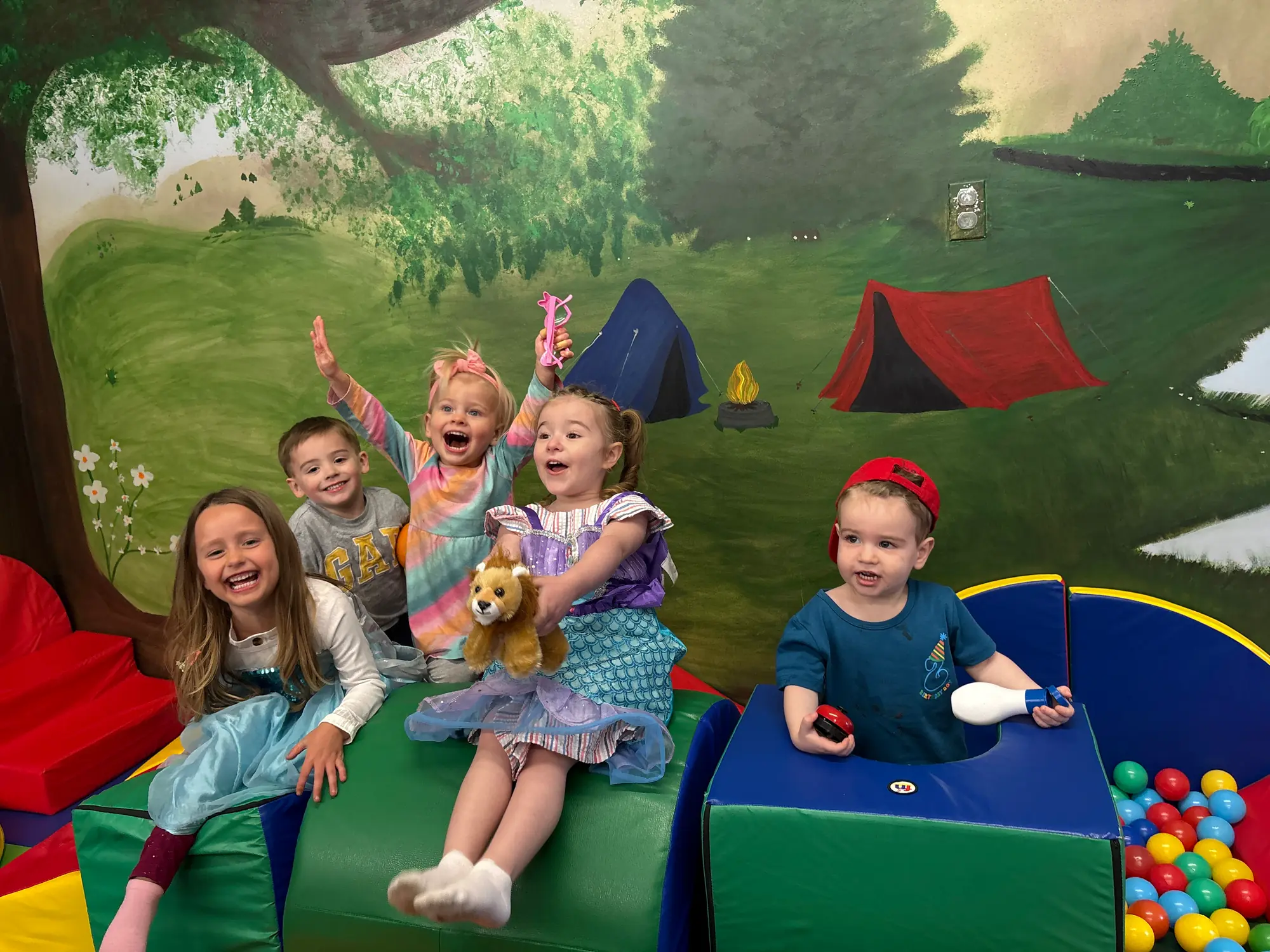 Children smiling and playing in front of the whimsical camp mural
