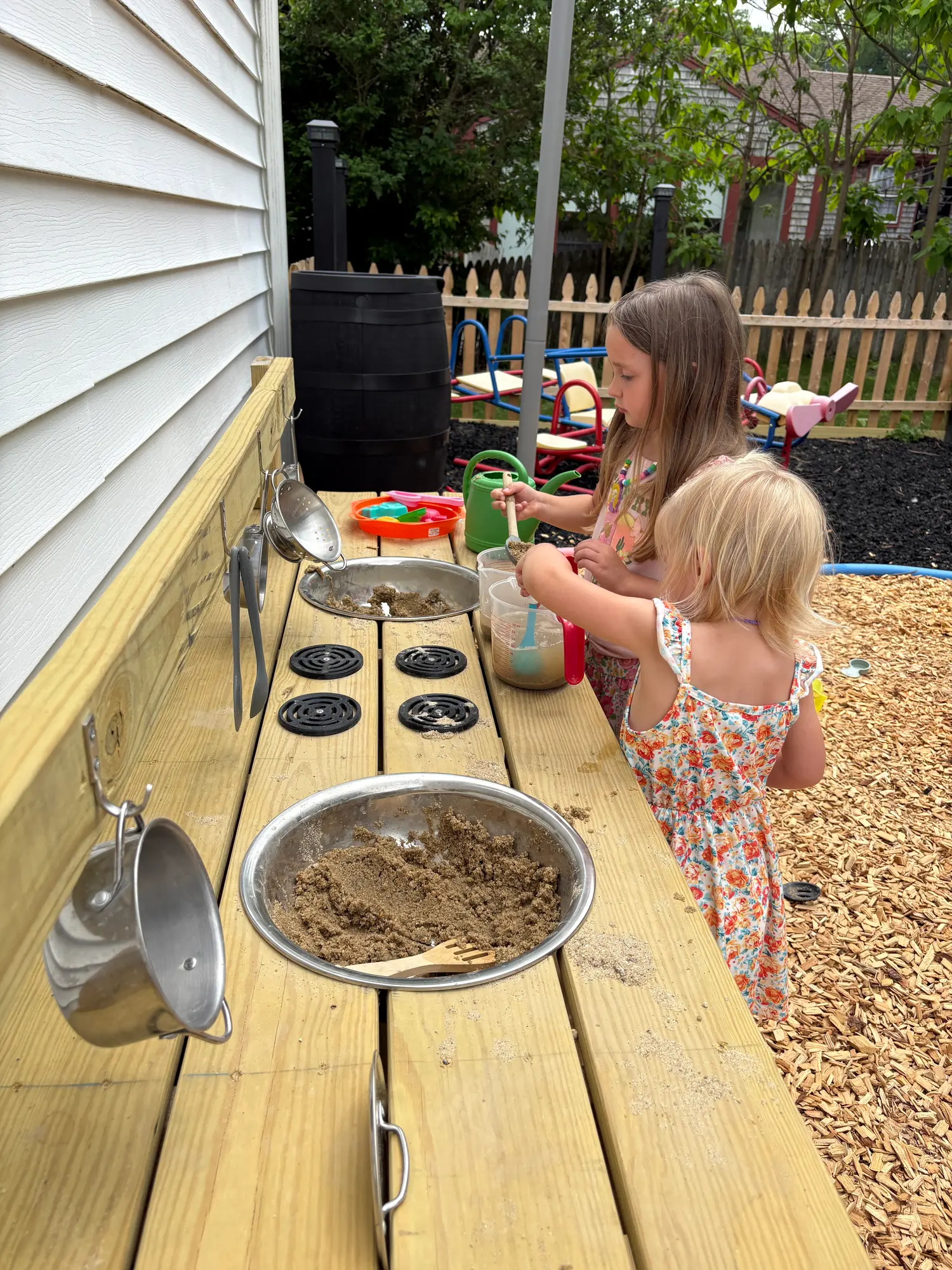Children playing at the outdoor mud kitchen in the fenced back yard