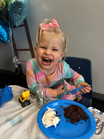 A child laughing while eating a slice of birthday cake