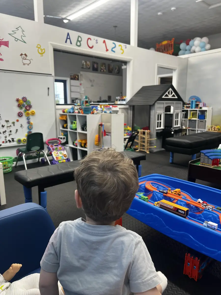 A child exploring the playroom with car tracks, gear walls, and indoor playhouse