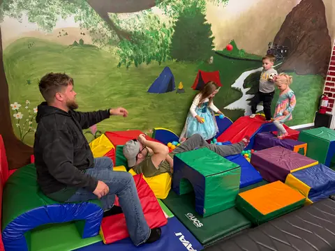 A parent playing with children in the soft-play area under the camping mural